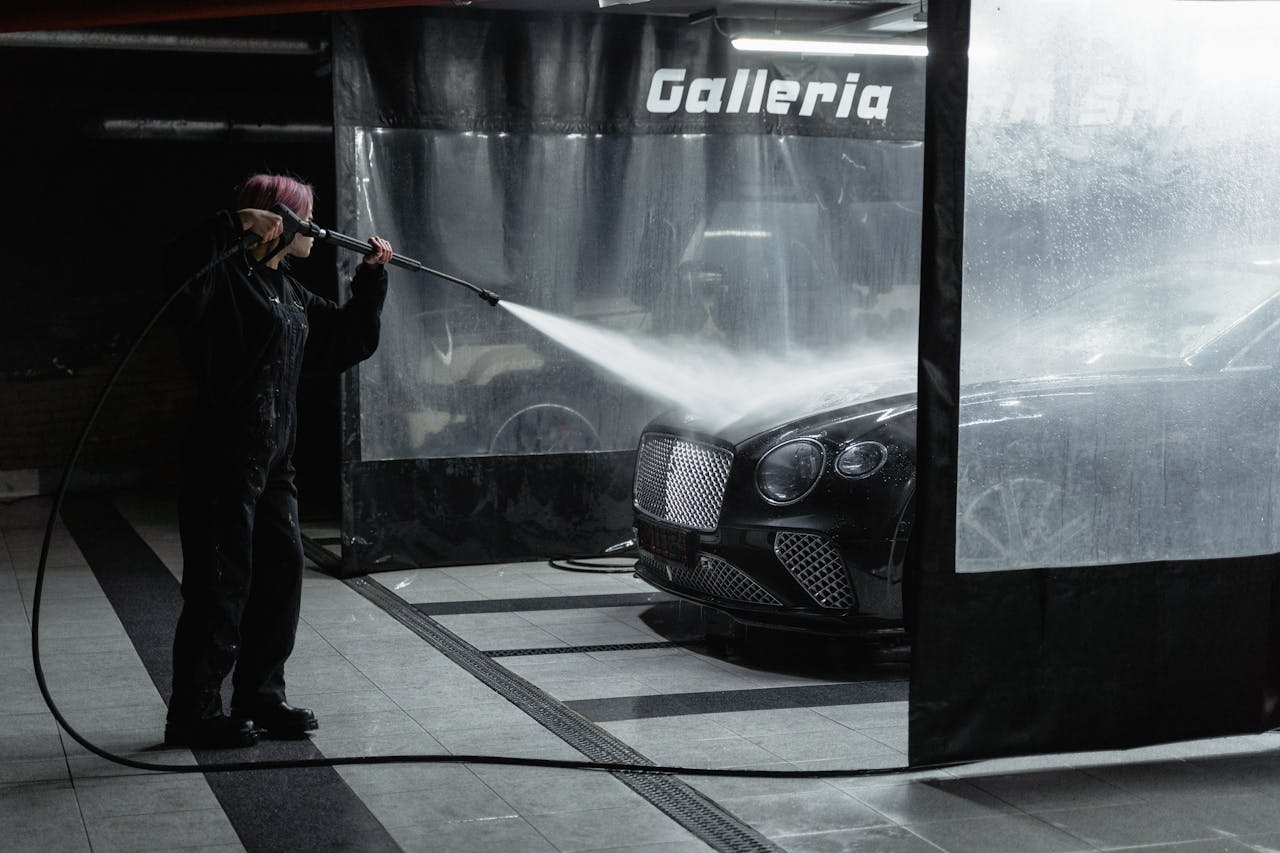 A woman power washing a luxury car in an indoor garage setting, showcasing car wash service.